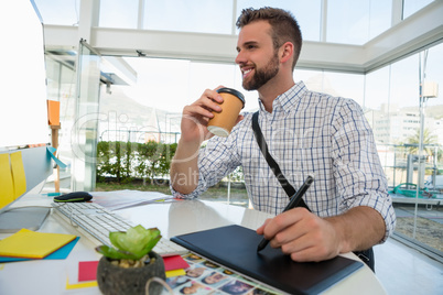 Designer having drink writing on graphic tablet at desk