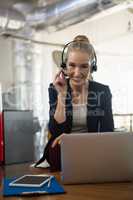 Portrait of businesswoman talking through headset while using laptop in office