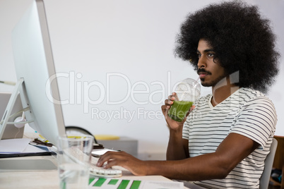 Man having drink while using computer in office