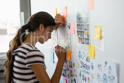 Tired woman leaning on wall with sticky notes in office