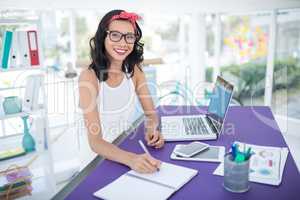 Smiling female executive writing in diary in office