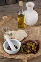 Olives with oil bottle and bread by spices in mortar pestle on table