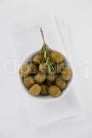 Overhead view of green olives with rosemary in bowl