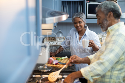 Smiling woman with coffee cup standing by man preparing food