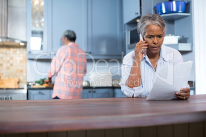 Worried woman reading document while standing in kitchen