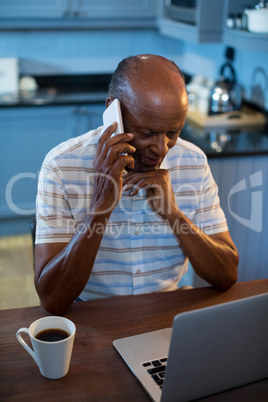 High angle view of man talking on phone while using laptop