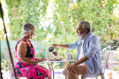 Senior man pouring coffee while sitting with woman in yard