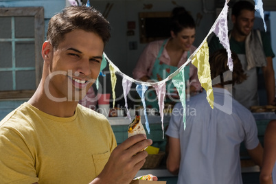 Young man eating tortilla while standing by food truck