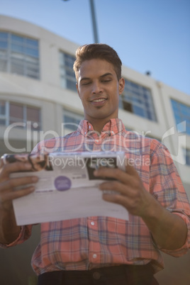 Low angle view of man reading paper while standing by building