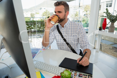 Designer having drink writing on graphics tablet