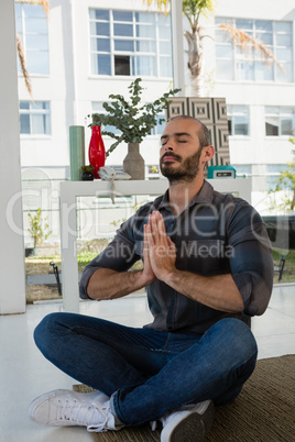 Businessman in prayer position meditating while sitting on floor