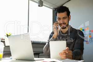 Man talking on phone while using tablet at office