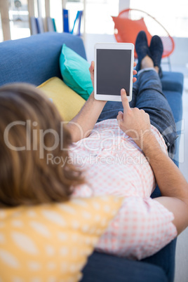 Male executive using digital tablet while relaxing on sofa