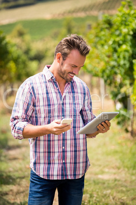 Young man using phone and tablet at vineyard