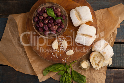 Black olives by garlic and herb by bread on cutting board