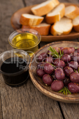 Close up of olives by oil in container with bread in background