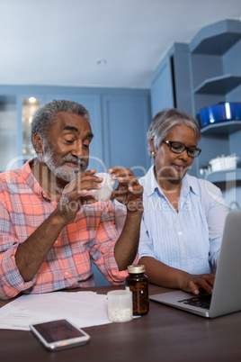 Man looking at medicine while sitting by woman using laptop computer