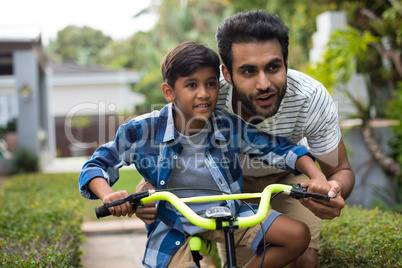 Father looking away while assisting son for cycling