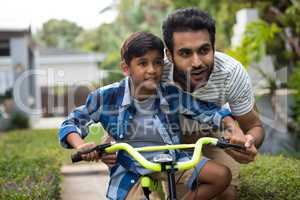 Father looking away while assisting son for cycling