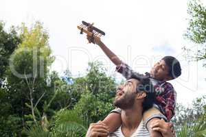 Boy playing with airplane while sitting on fathers shoulder