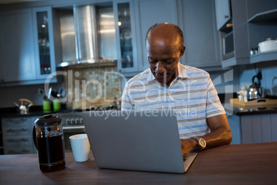 Senior man using laptop at table in kitchen