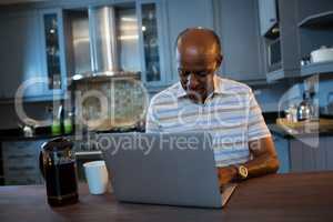 Senior man using laptop at table in kitchen