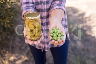 Mid section of woman holding pickled jar and harvested olives