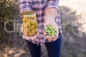 Mid section of woman holding pickled jar and harvested olives