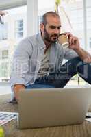 Designer holding disposable cup using laptop while sitting on floor