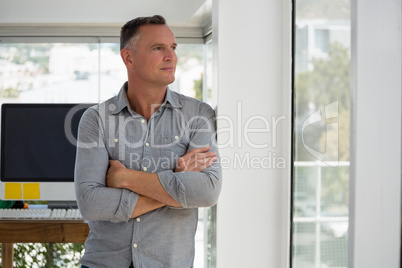 Confident businessman looking through window while leaning on wall