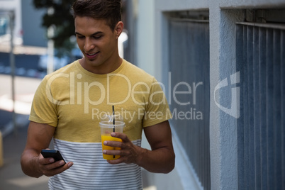 Smiling young man having juice while using mobile phone