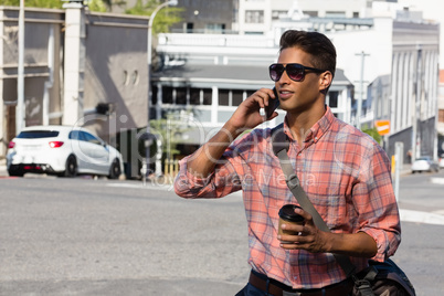 Young man in sunglasses talking on mobile phone on city street