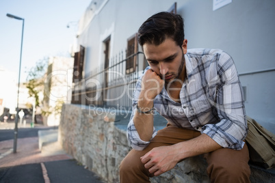 Tensed man looking down while sitting on retaining wall