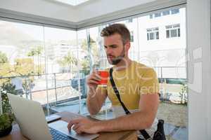 Businessman having drink while using laptop at desk