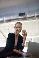 Businesswoman holding disposable cup while sitting with laptop at table