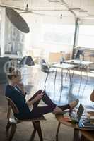 Businesswoman using phone while relaxing on chair at office