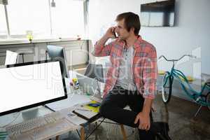 Businessman talking on phone while sitting on desk