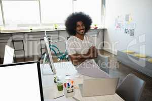Portrait of smiling man sitting on desk at office