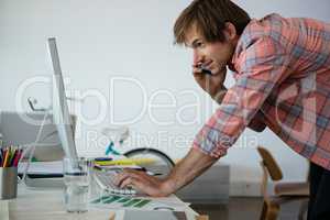 Man talking on phone while using computer at desk