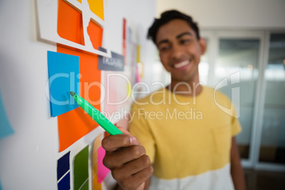 Smiling man pointing at sticky notes with felt tip pen in office