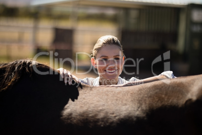 Smiling woman standing with a brown horse in the ranch