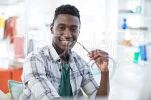 Smiling male executive holding spectacles in office