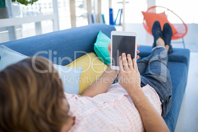 Male executive using digital tablet while relaxing on sofa Male executive using digital tablet while relaxing on sofa