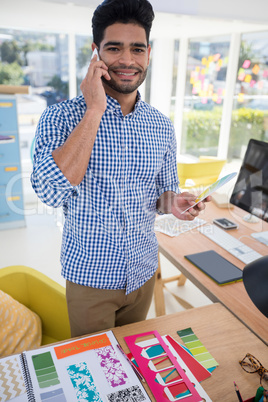 Male graphic designer talking on mobile phone at desk