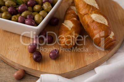 Olives in container by bread on cutting board