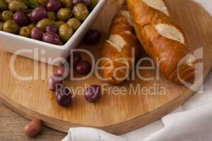 Olives in container by bread on cutting board