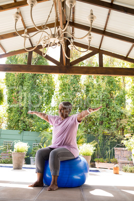 Full length of senior woman with arms outstretched sitting on exercise ball
