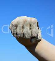 Male fist smeared with mud on blue sky background