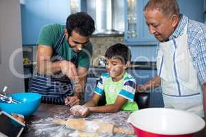 Father sprinkling flour on son hand while preparing food with grandfather