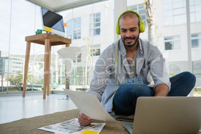 Smiling desginer holding collage using laptop while sitting on floor